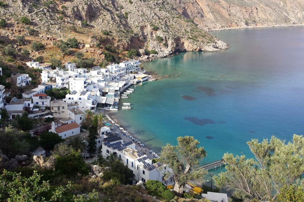 Paysage d'une baie avec des maisons blanches en contrebas, entouré de reliefs montagneux et face à l'eau turquoise de Crète.