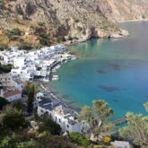 Paysage d'une baie avec des maisons blanches en contrebas, entouré de reliefs montagneux et face à l'eau turquoise de Crète.