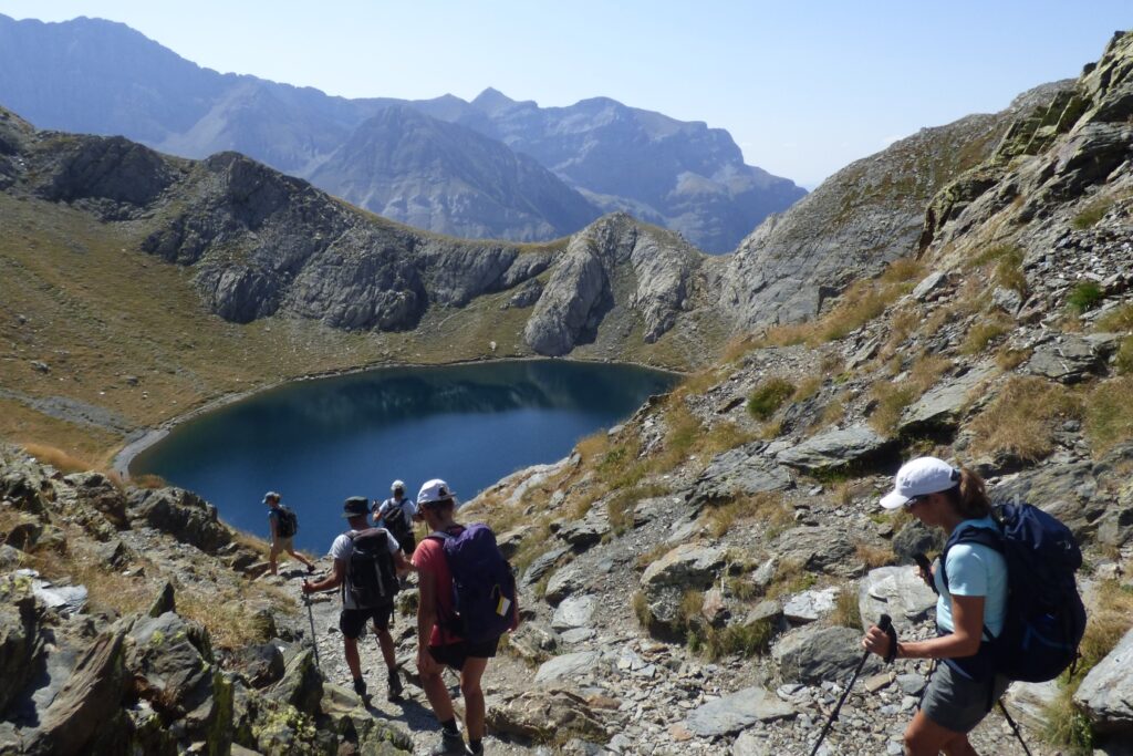 Groupe de randonneurs sur un sentier avec leur guide se dirigeant vers un lac de montagne entouré de sommets