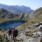 Groupe de randonneurs sur un sentier avec leur guide se dirigeant vers un lac de montagne entouré de sommets