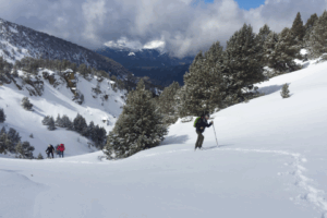Paysage avec un randonneur en raquette qui monte le flanc d'une montagne, suivi d'un groupe de randonneurs en raquettes dans la neige