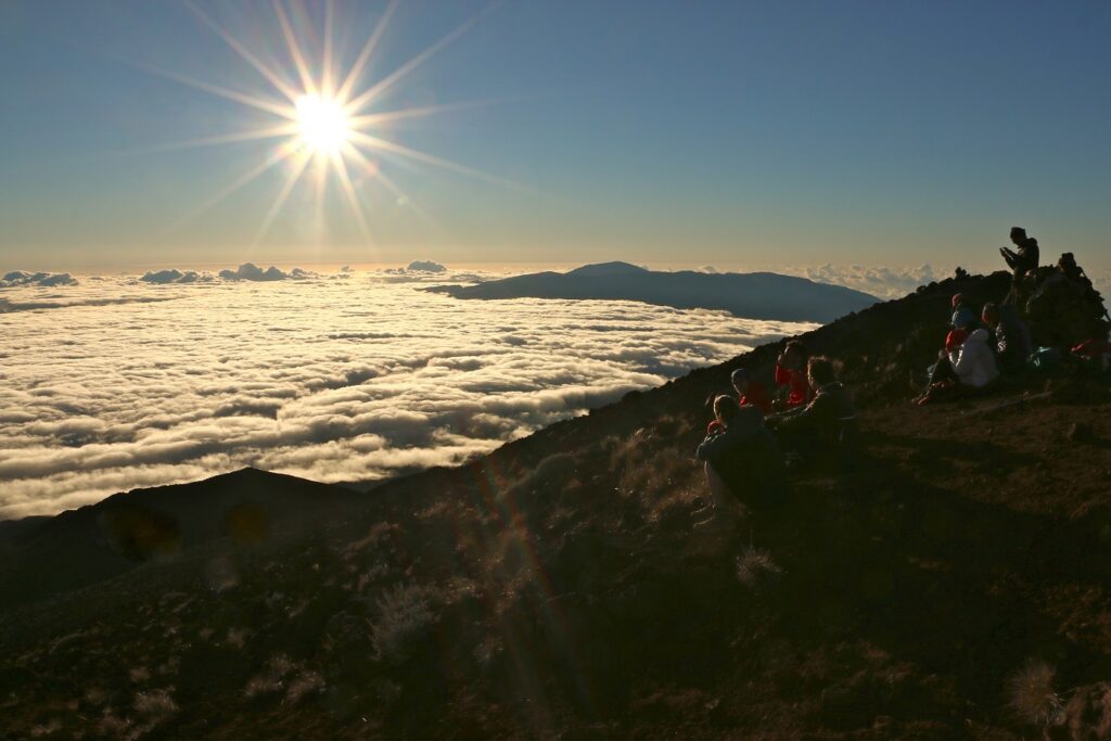 Paysage de montagne avec le soleil, ainsi qu'une mer de nuages et un groupe de randonneurs qui observe cette vue