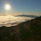 Paysage de montagne avec le soleil, ainsi qu'une mer de nuages et un groupe de randonneurs qui observe cette vue