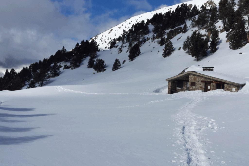 Paysage hivernal avec une trace du groupe en raquette dans la neige et une maison en pierre dans le fond.