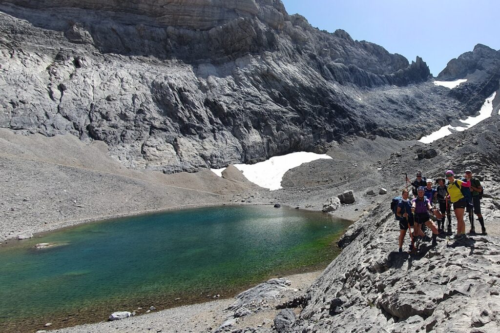 Groupe de montagnards face à un lac de montagne encadré de sommets et présentant encore de la neige par endroit