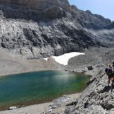 Groupe de montagnards face à un lac de montagne encadré de sommets et présentant encore de la neige par endroit