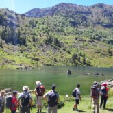 Groupe de randonneurs avec leur guide face à un lac de montagne et des sommets qui leur font face