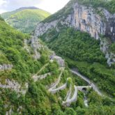 Paysage de montagne avec des falaises ainsi qu'une route qui passe à flanc de la montagne en formant des lacets