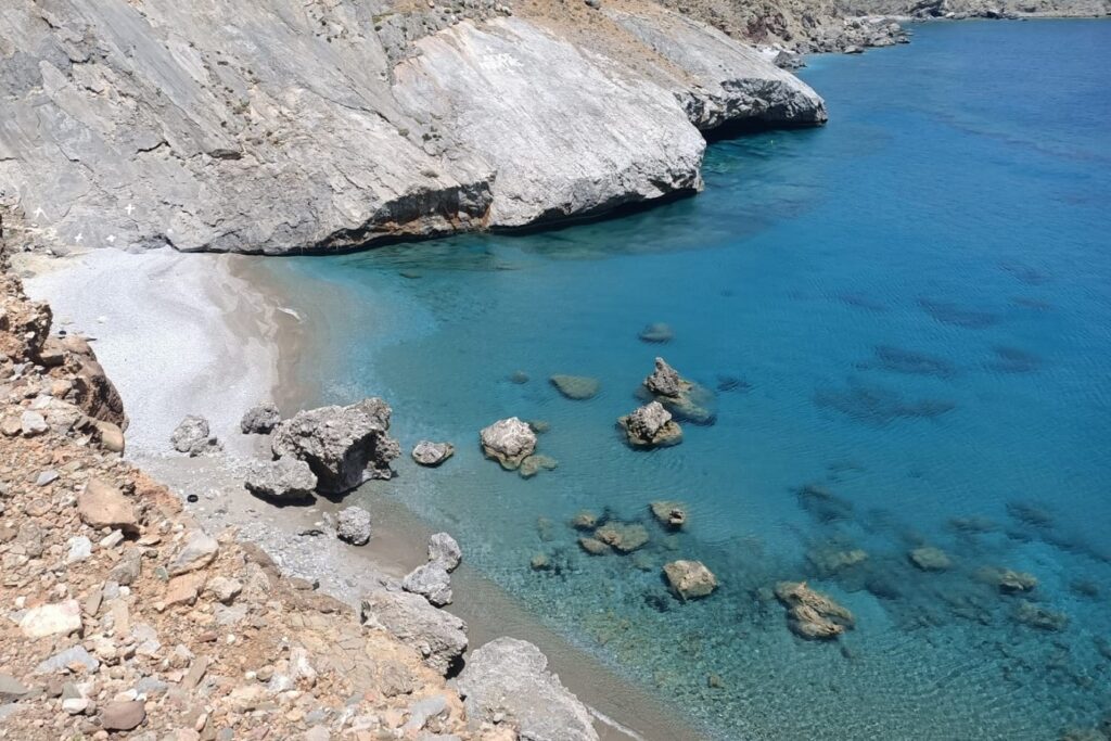 Paysage de bord de mer en Crète avec de l'eau bleu turquoise encadré d'une plage de cailloux et avec des rochers