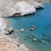 Paysage de bord de mer en Crète avec de l'eau bleu turquoise encadré d'une plage de cailloux et avec des rochers