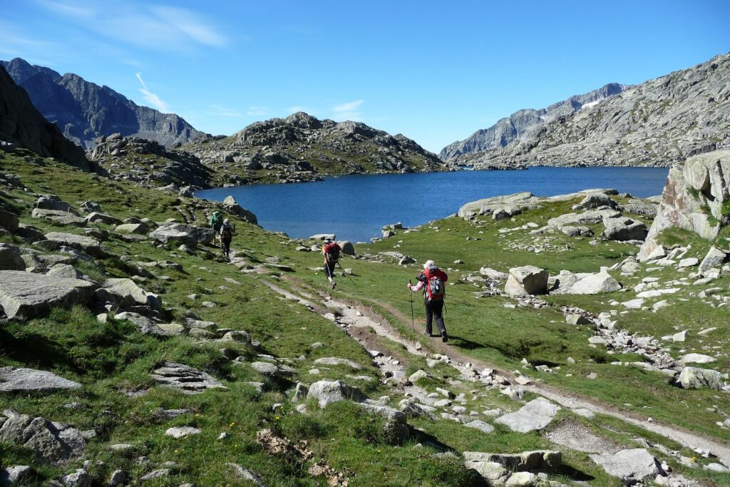 groupe de randonneurs sur un sentier se dirigeant dans les encantats, vers un lac de montagne, avec un paysage d'été et des sommets en fond
