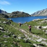 groupe de randonneurs sur un sentier se dirigeant dans les encantats, vers un lac de montagne, avec un paysage d'été et des sommets en fond