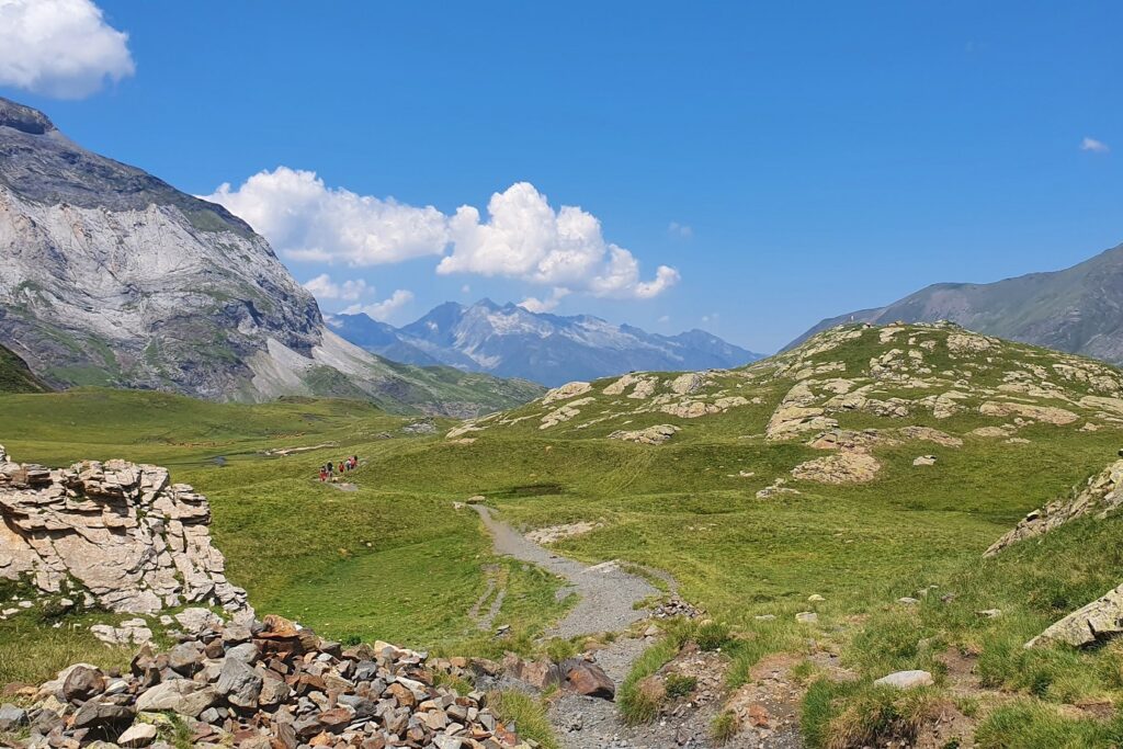 Paysage de montagne avec des sentiers à travers des plaines recouvertes de végétation et des sommets en fond