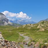 Paysage de montagne avec des sentiers à travers des plaines recouvertes de végétation et des sommets en fond