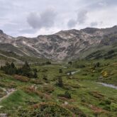 Paysage montagneux avec une plaine et des arbres, ainsi que les sentiers du GR 10 et en fond des sommets
