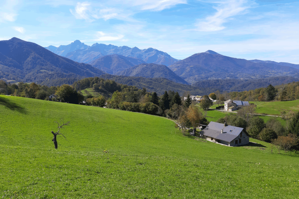Paysage verdoyant avec en contrebas une maison au toit d'ardoise et une belle vue sur les différents sommets en arrière-plan