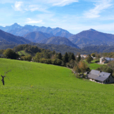 Paysage verdoyant avec en contrebas une maison au toit d'ardoise et une belle vue sur les différents sommets en arrière-plan
