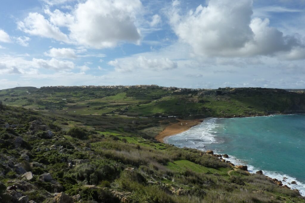 Paysage côtier à Malte avec une plage et de l'eau turquoise qui sort du lot, encadré par de grandes forêts