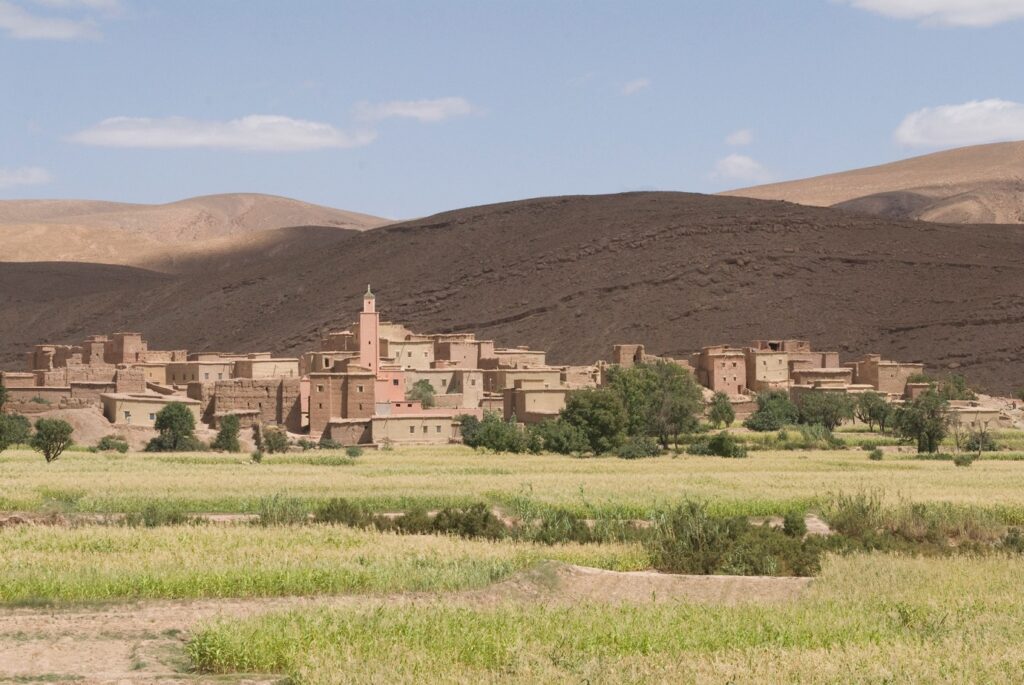Paysage marocain avec un village à l'arrière-plan ainsi que des reliefs montagneux et de la végétation au premier plan
