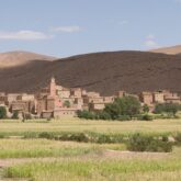 Paysage marocain avec un village à l'arrière-plan ainsi que des reliefs montagneux et de la végétation au premier plan
