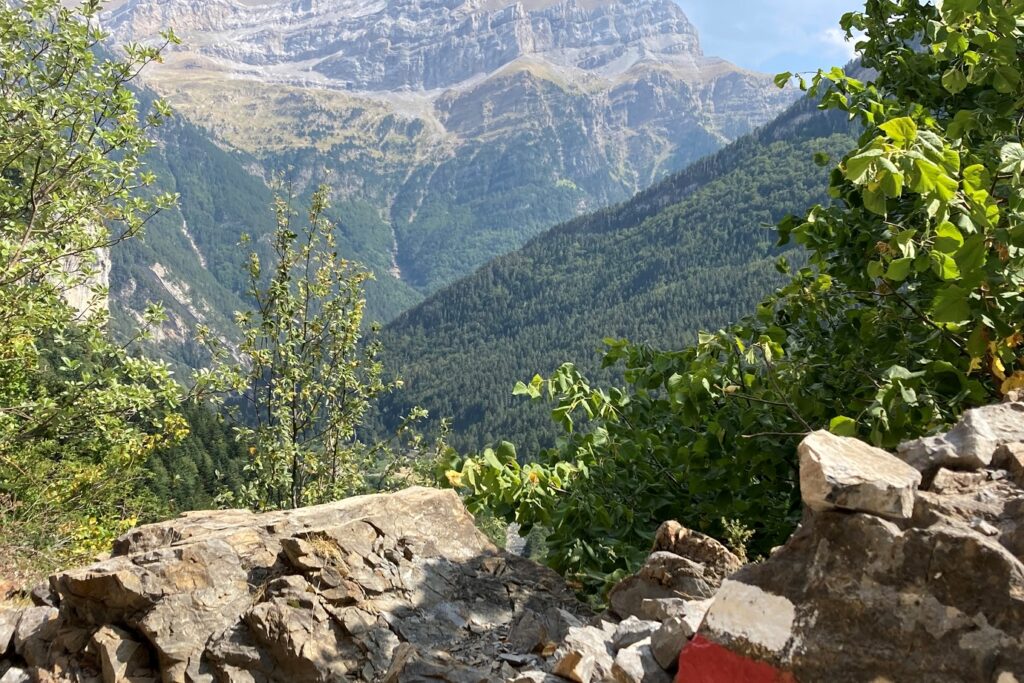 Paysage avec en fond les sommets dans la zone de Ordesa et au premier plan des roches, notamment une balisée signalant le chemin