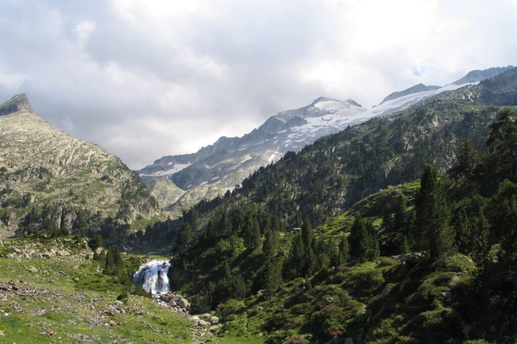 Paysage randonnée à l'Aneto accompagnée par un guide, où l'on peut observer une cascade dans le premier plan et plus haut des montagnes couvertes de neige.