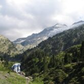 Paysage randonnée à l'Aneto accompagnée par un guide, où l'on peut observer une cascade dans le premier plan et plus haut des montagnes couvertes de neige.