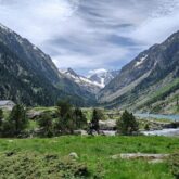 Paysage montagnard avec des sommets en fond et au premier plan un plateau avec des arbre et un cours d'eau