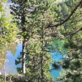 Lac de montagne observé à travers les arbres d'une forêt des Encantats lors d'un séjour de découverte de ce domaine.