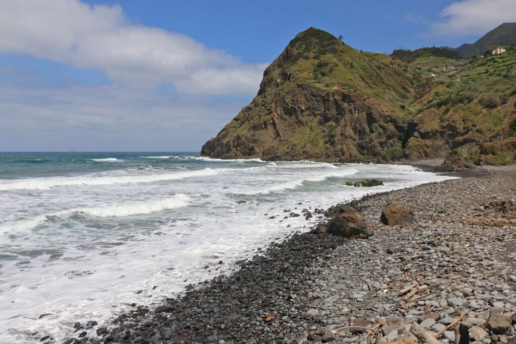 Plage de Madère avec des cailloux noirs sur la plage et un sommet en face, on voit aussi l'océan.