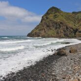 Plage de Madère avec des cailloux noirs sur la plage et un sommet en face, on voit aussi l'océan.