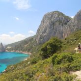 Groupe de randonneurs sur un sentier de randonnée en Sardaigne, parallèlement à ce sentier côtier, on voit la mer sur la gauche et des sommets en fond
