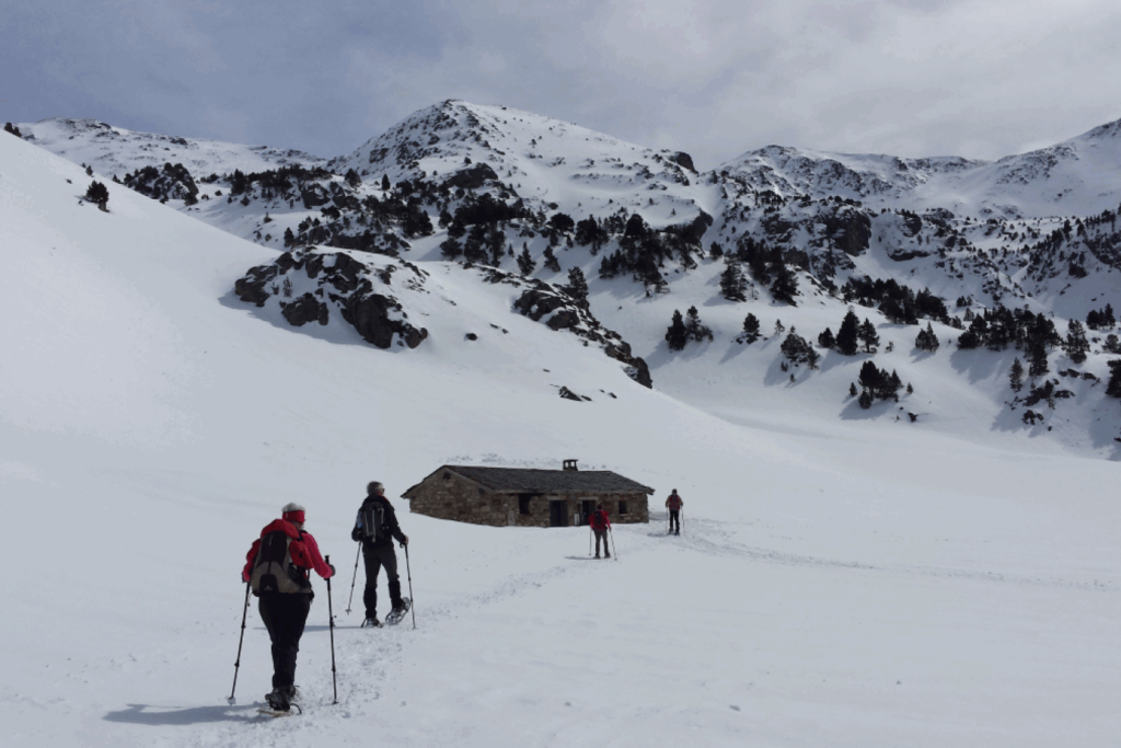 Groupe de marcheurs se dirigeant vers une cabane en pierre dans une étendue de neige avec un fond montagneux.