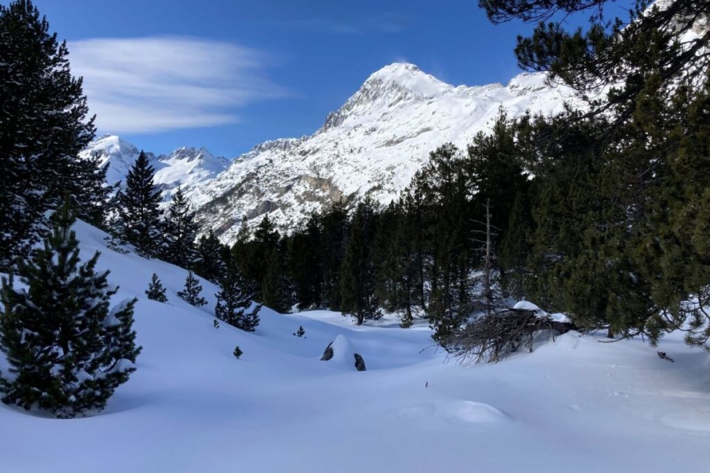 Paysage hivernal dans les Pyrénées proche de l'Aneto, avec en fond un sommet à la lumière du soleil couvert de neige.