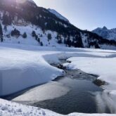 paysage hivernal avec un ruisseau entouré de neige et avec au fond des montagnes couvertes de forêts