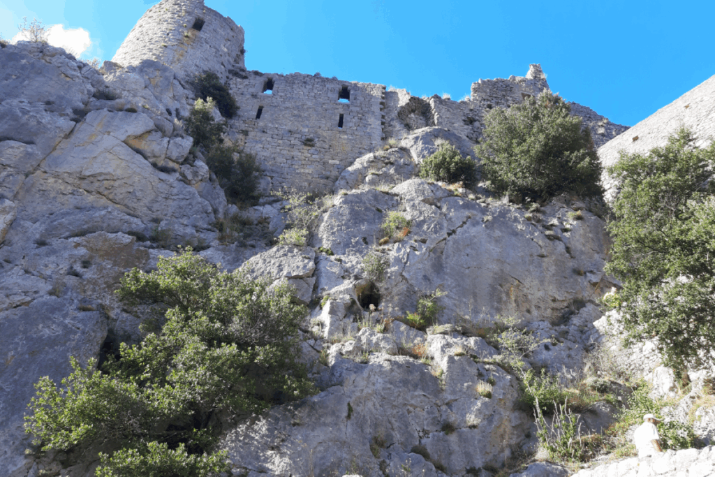 Château cathare en contrebas, entouré de falaises et de verdure, paysage estival.