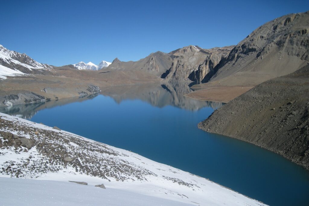 Paysage de montagne avec un lac au centre et des parties de montagnes contenant encore des traces de neige