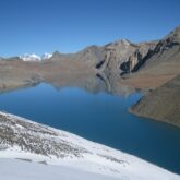 Paysage de montagne avec un lac au centre et des parties de montagnes contenant encore des traces de neige