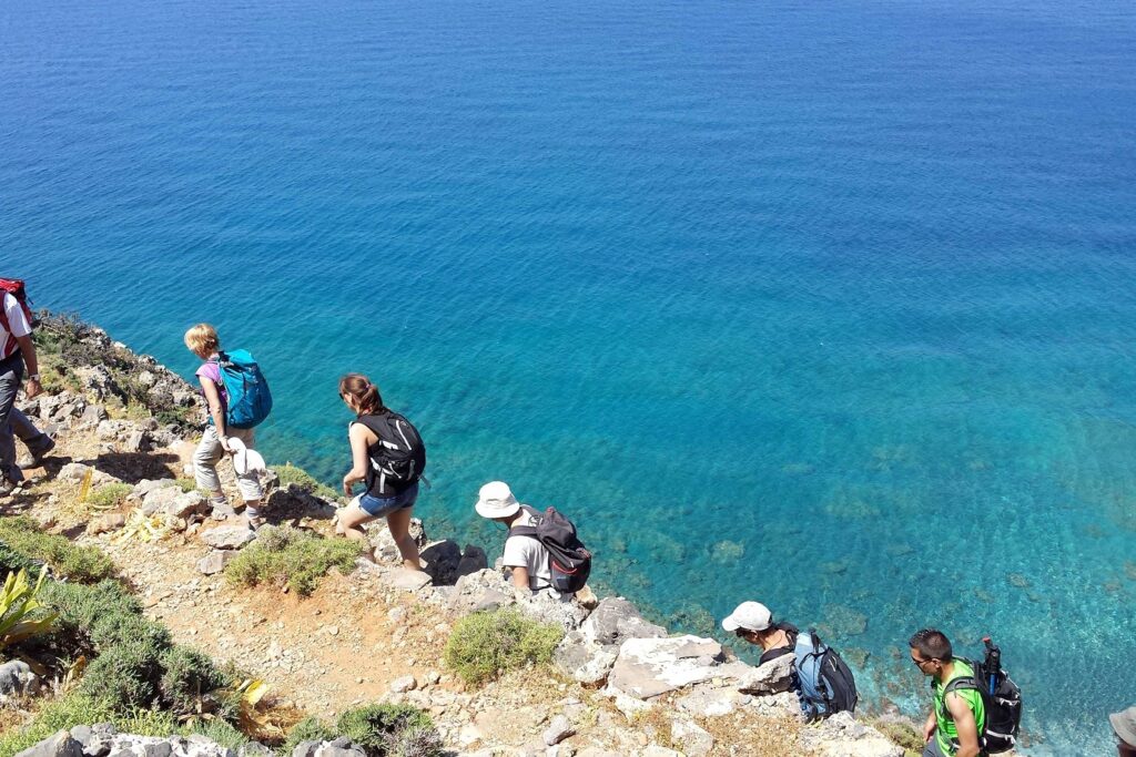 Groupe de randonneurs pris de haut sur un sentier côtier avec à leur droite la mer, l'eau a des couleurs turquoises, cette scène se déroule en Crète