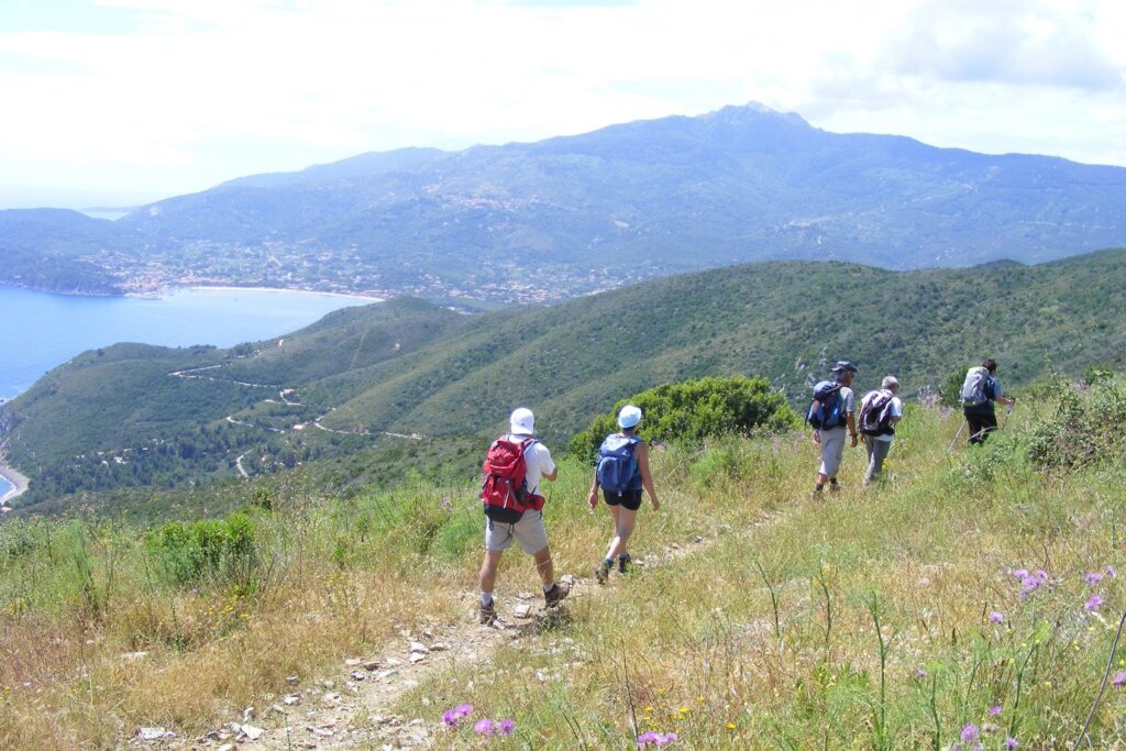 Groupe de randonneurs sur un sentier côtier avec vue sur la mer à gauche et depuis la montagne