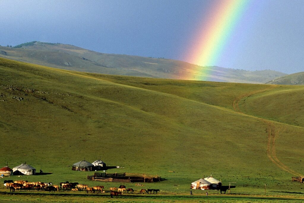 Paysage montagnard avec un arc-en-ciel au milieu de la plaine et une yourte en contrebas avec un troupeau.