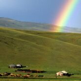 Paysage montagnard avec un arc-en-ciel au milieu de la plaine et une yourte en contrebas avec un troupeau.