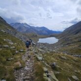 Groupe de randonneurs sur un sentier qui s'avancent, avec leur guide, vers un lac de montagne