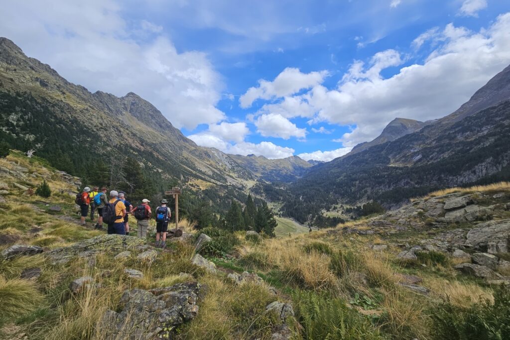 Groupe de randonneurs face au paysage montagnard estival et un panneau leur indiquant leur chemin au cours du tour des Posets avec leur guide