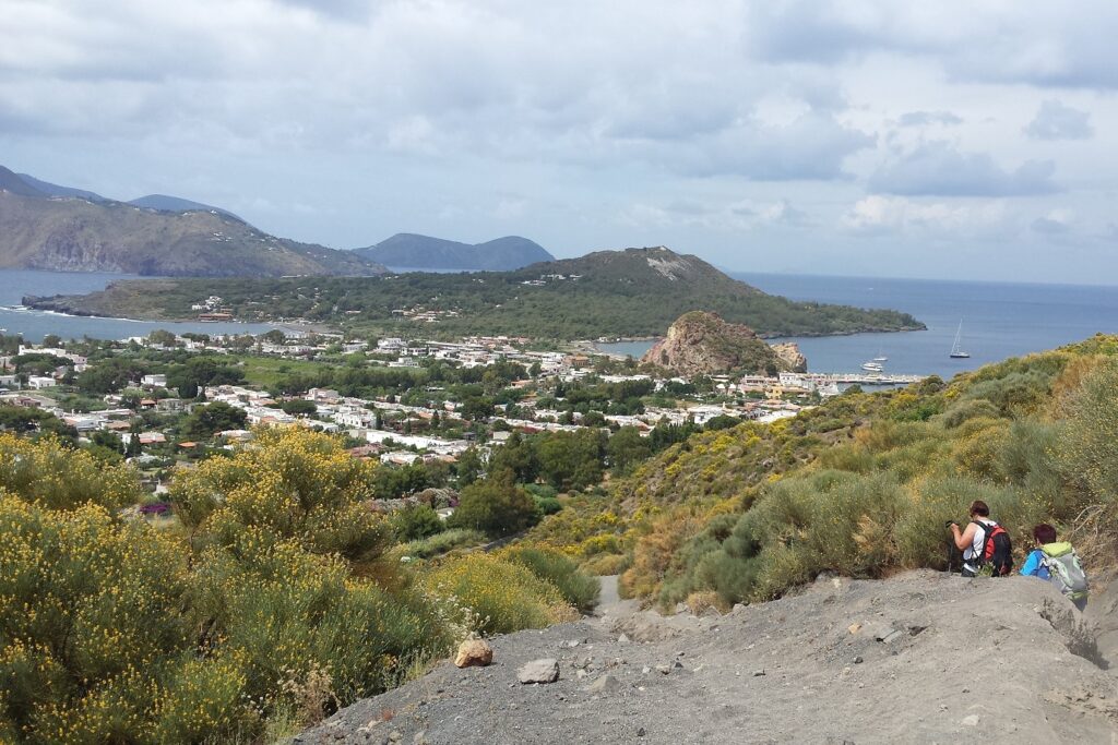 Paysage des îles éoliennes avec des volcans en fond, la mer sur la droite ainsi que de la végétation sur les hauteurs et un village en contrebas