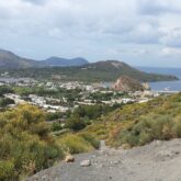 Paysage des îles éoliennes avec des volcans en fond, la mer sur la droite ainsi que de la végétation sur les hauteurs et un village en contrebas