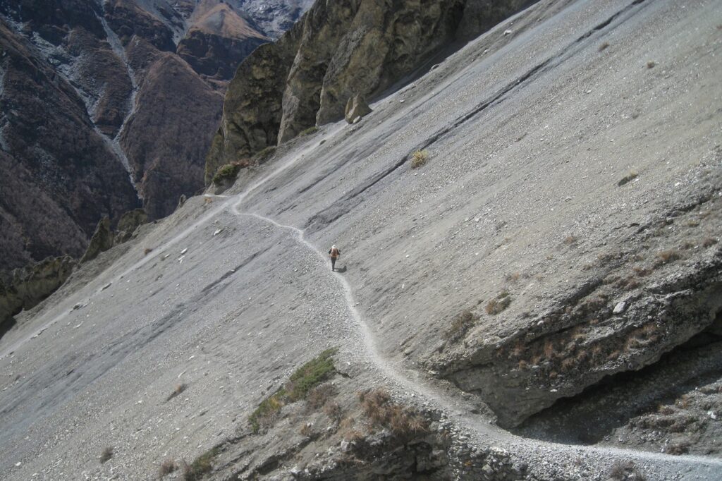 Prise de vue en contrebas d'un flanc de montagne sur lequel on voit un sentier emprunté par des randonneurs lors du tour des Annapurna