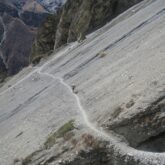 Prise de vue en contrebas d'un flanc de montagne sur lequel on voit un sentier emprunté par des randonneurs lors du tour des Annapurna