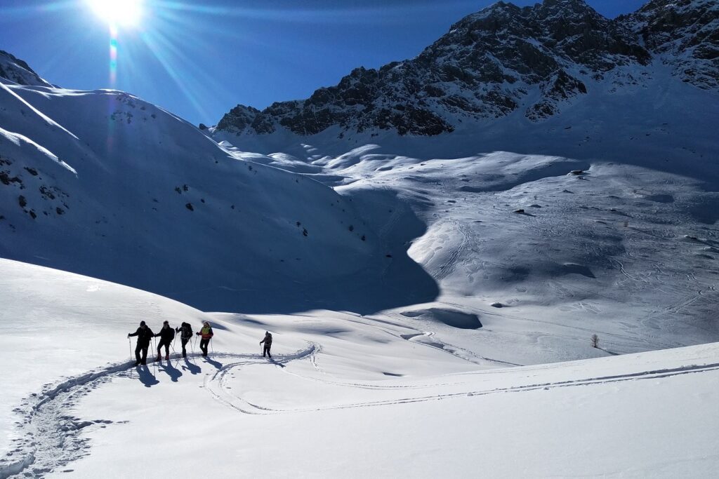 Paysage de montagne avec un grand soleil et un groupe de randonneurs accompagné d'un guide de randonnée dans le massif du Queyras