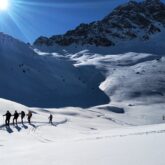 Paysage de montagne avec un grand soleil et un groupe de randonneurs accompagné d'un guide de randonnée dans le massif du Queyras